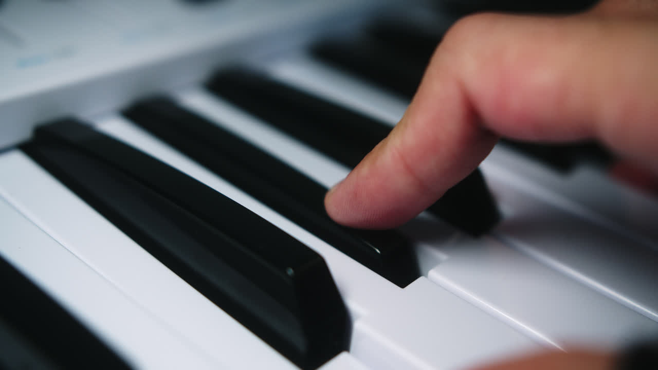 Beautiful slow motion shot of a professional musician's hands playing chords on a midi controller piano in his home studio.