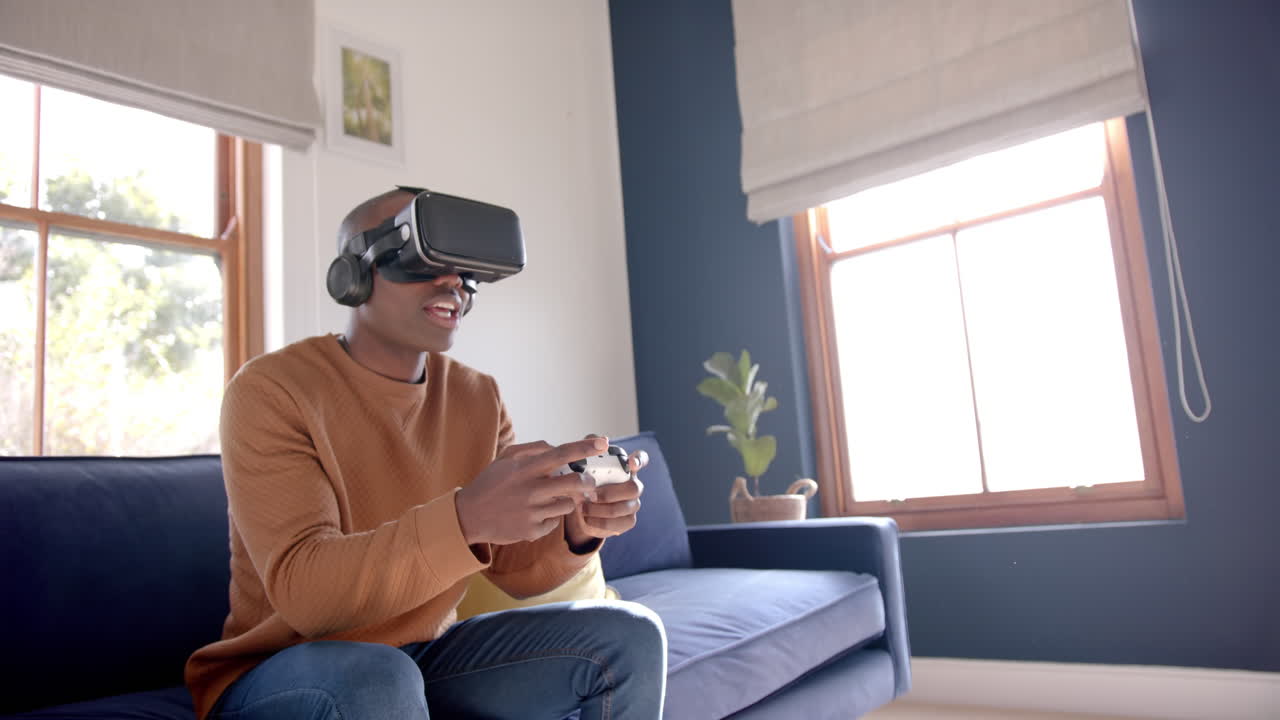 Uomo afroamericano che gioca a un videogioco usando un visore VR a casa, al rallentatore.