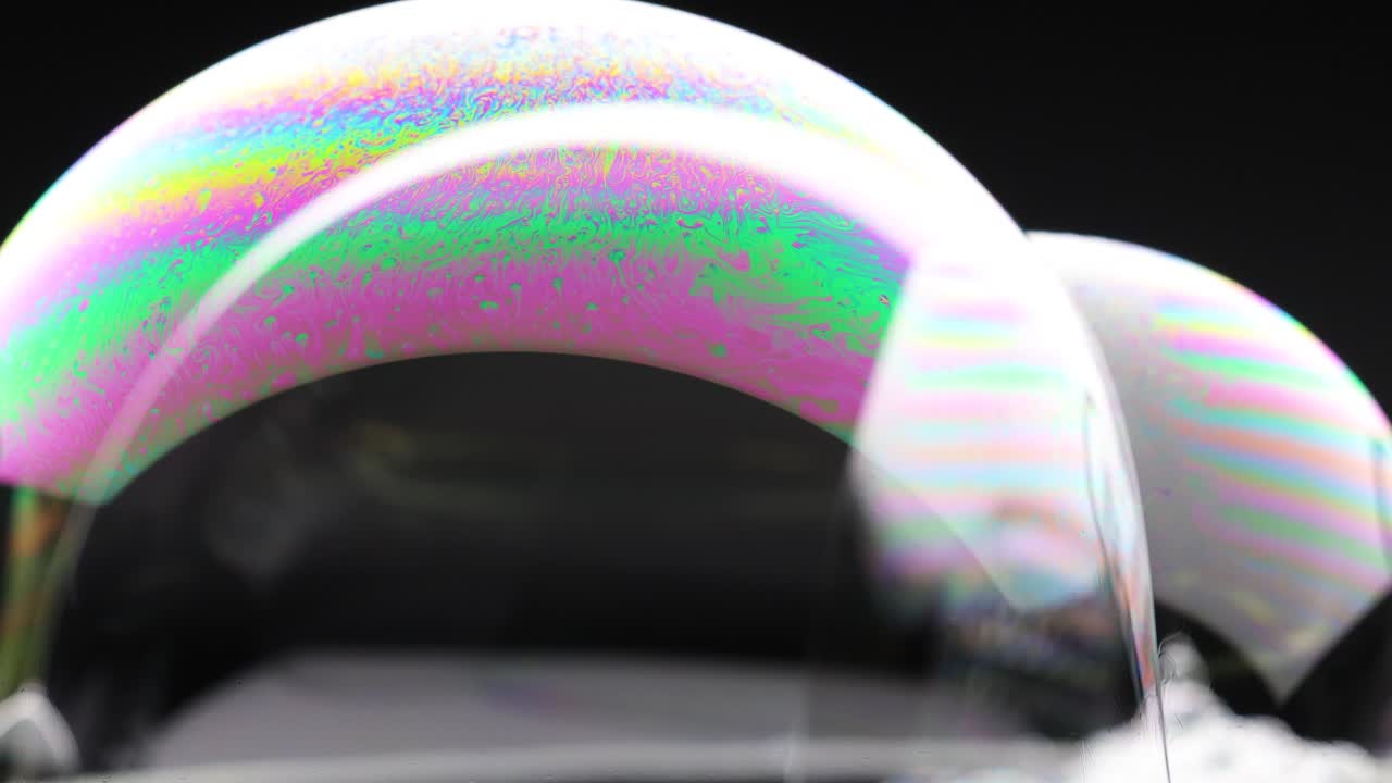 Vibrant soap bubbles display shifting colors and reflections against a dark background, creating a mesmerizing visual effect