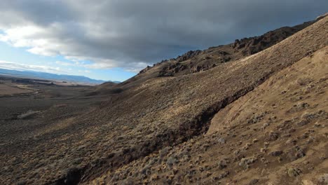 aerial drone forward moving shot over barren desert mountain slope dotted with small shrubs on a cloudy day