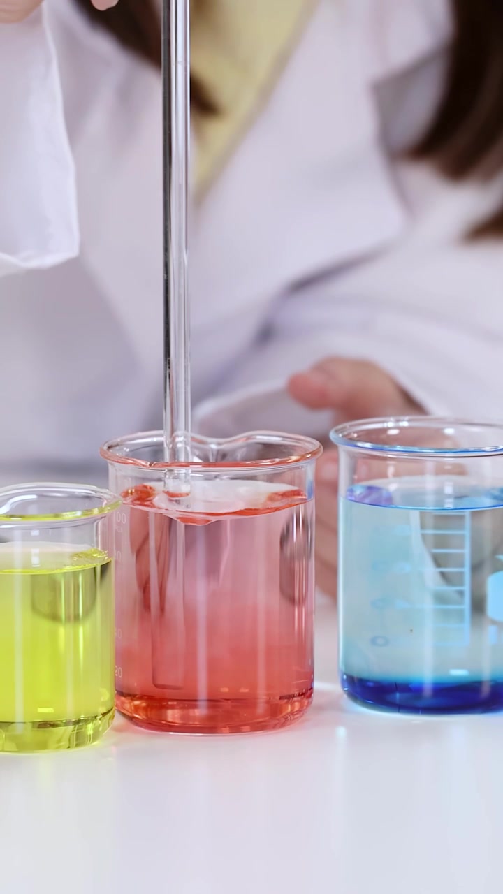 Primo piano di uno scienziato in camice bianco da laboratorio che mescola soluzioni chimiche colorate in becher