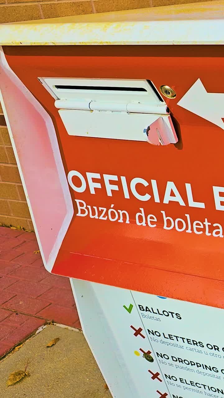 Una cassetta postale verticale per schede elettorali, chiaramente contrassegnata in inglese e spagnolo come "Official Ballot Drop Box, Buzón de Boleta Oficial", si trova all'esterno come luogo sicuro per la consegna delle schede elettorali.