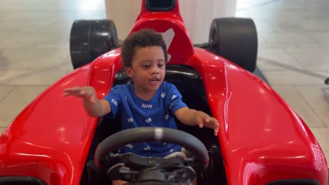 joyful scene: 3-year-old very expressive black child enjoying in a red f1 simulator inside a mall