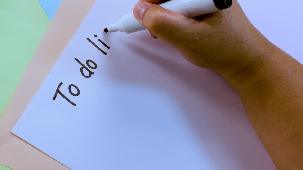 Person writes 'To do list!' and draws checkboxes on white paper under soft lighting