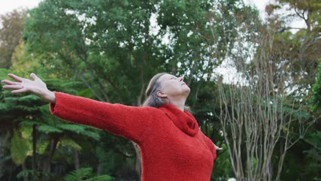 happy senior caucasian woman standing stretching in garden, relaxing with eyes closed