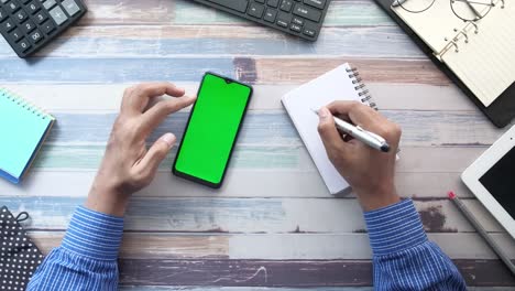 person using smartphone and taking notes at a desk