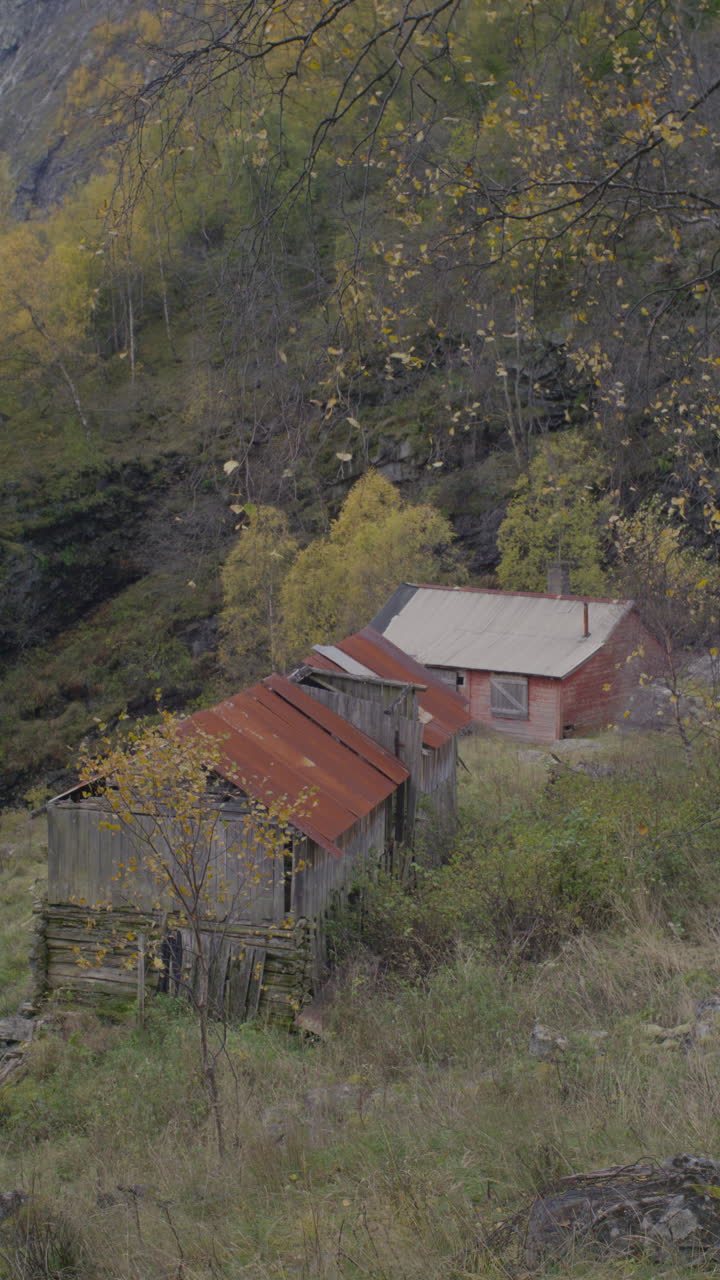 Old wooden farm houses with rusted roofs stand abandoned in a rural autumn setting with trees. Filmed on a mountainside in Nundalen, on the west coast of Norway.