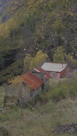 old wooden farm houses with rusted roofs stand abandoned in a rural autumn setting with trees. filmed on a mountainside in nundalen, on the west coast of norway.