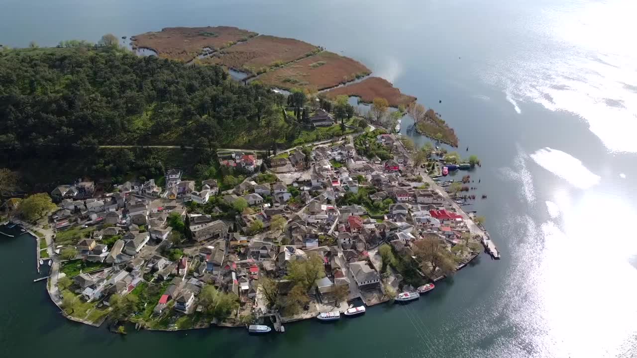 Yunanistan'daki Pamvotida Gölü üzerinde yer alan Yanya Adası'nın geleneksel yerleşim yerinin etrafında, taş evleri ve yeşil bitki örtüsünü gösteren, yumuşak bir yarım yörünge çizen havadan drone çekimi.