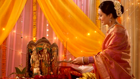 indian woman in saree worshipping ram darbar / family idols at home - puja festival celebration