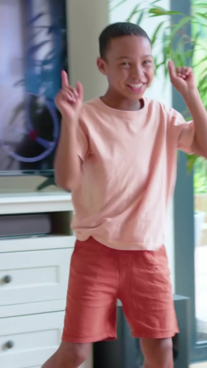 Vertical video: Tracking boy in pink shirt orange shorts rising at living room window for tracking