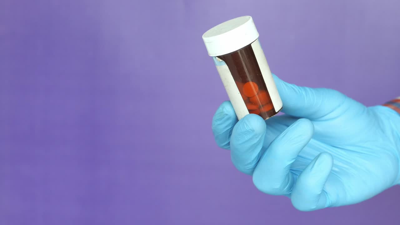Hand in Blue Gloves Holding a Medicine Bottle