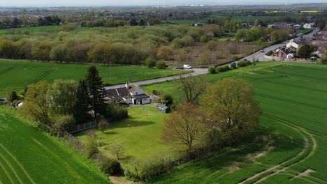 rural british farmhouse aerial view surrounded by lush green trees and agricultural farmland countryside fields, zoom in shot