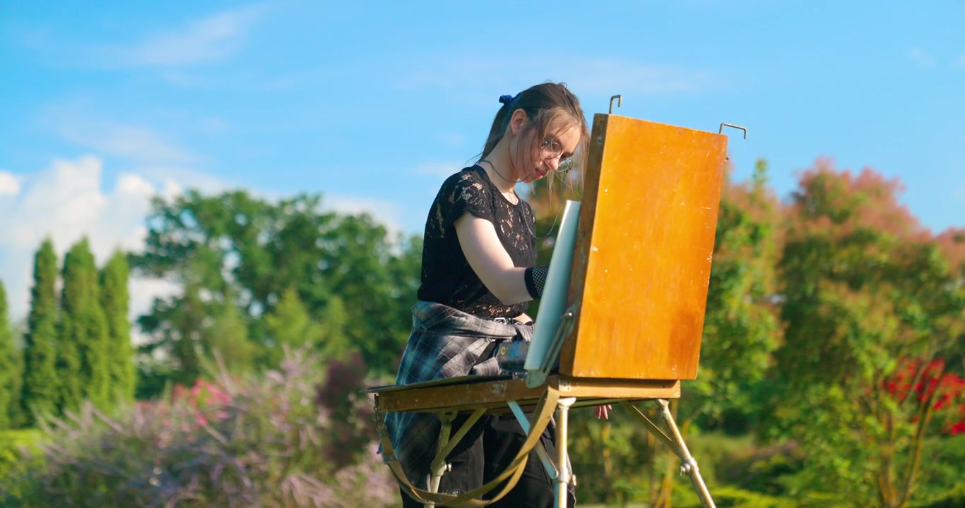 Giovane artista donna che dipinge su tela in un parco soleggiato