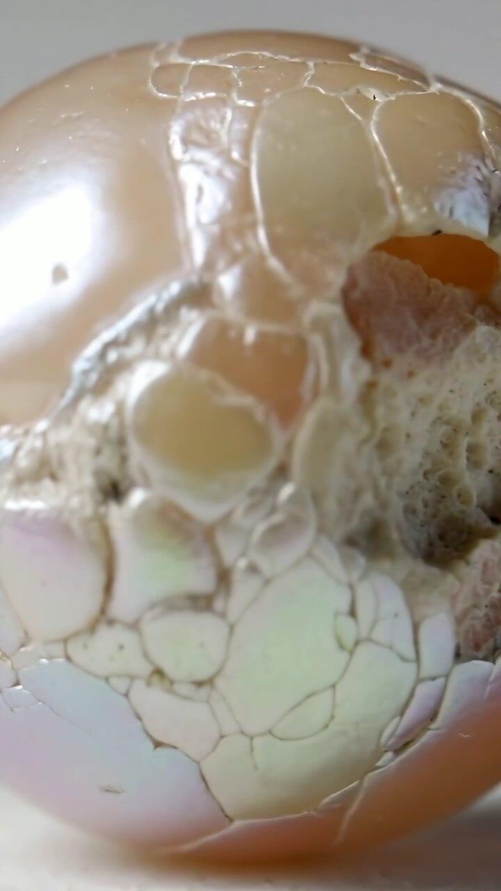 Vertical video: Rotating camera revealing pearl orb cracking on gray backdrop exposing porous core