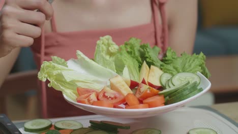 close up of woman's hands holding a dish and  using a fork poking carrots while sitting in the kitchen