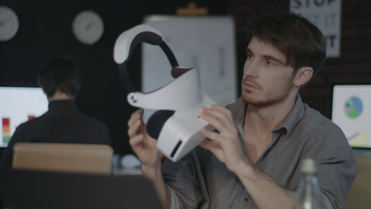 Giovane che tiene occhiali per realtà virtuale in ufficio scuro creativo