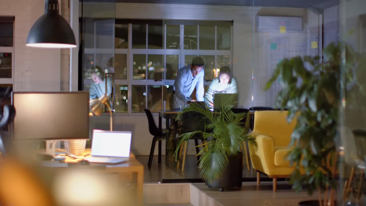 colegas masculinos y femeninos diversos discutiendo el trabajo usando tableta y portátil tarde en la oficina, espacio de copia