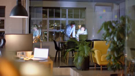 diverse male and female colleague discussing work using tablet and laptop late in office, copy space