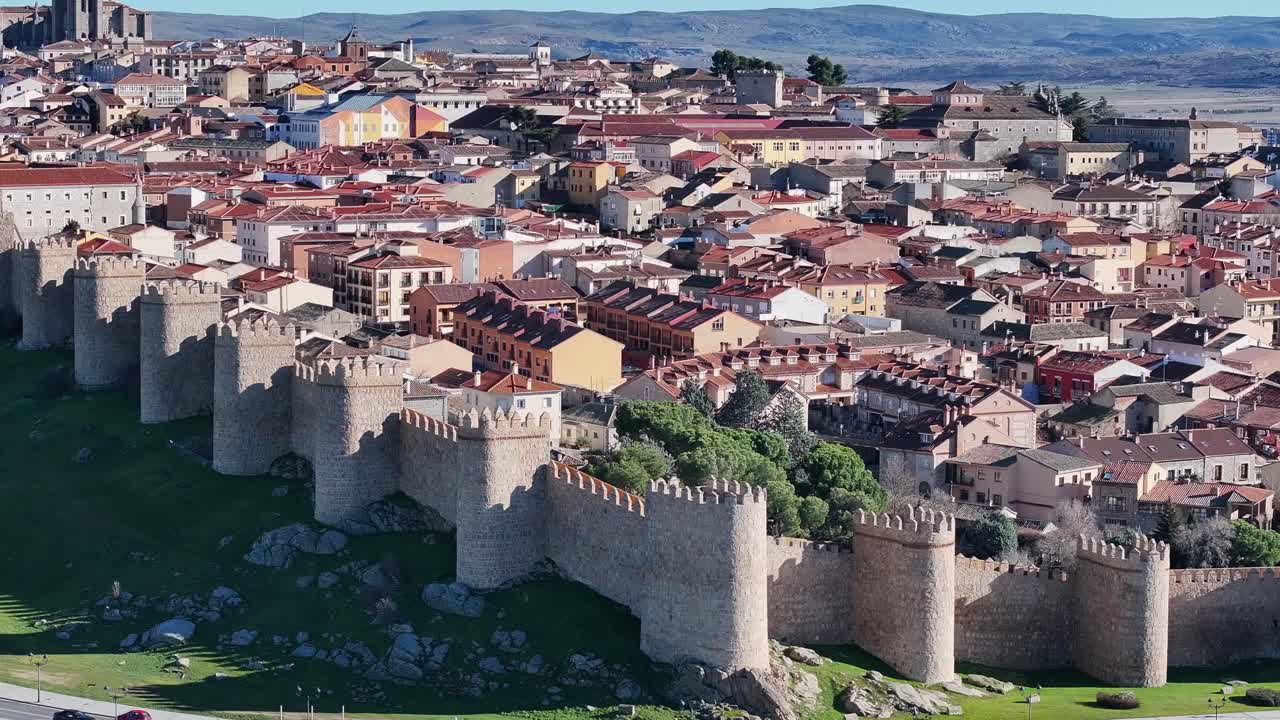 70 mm filmando con un dron sobre la ciudad amurallada de ávila, visualizando los techos de las casas, las paredes de piedra y sus torres, una carretera con vehículos y sus montañas en el fondo