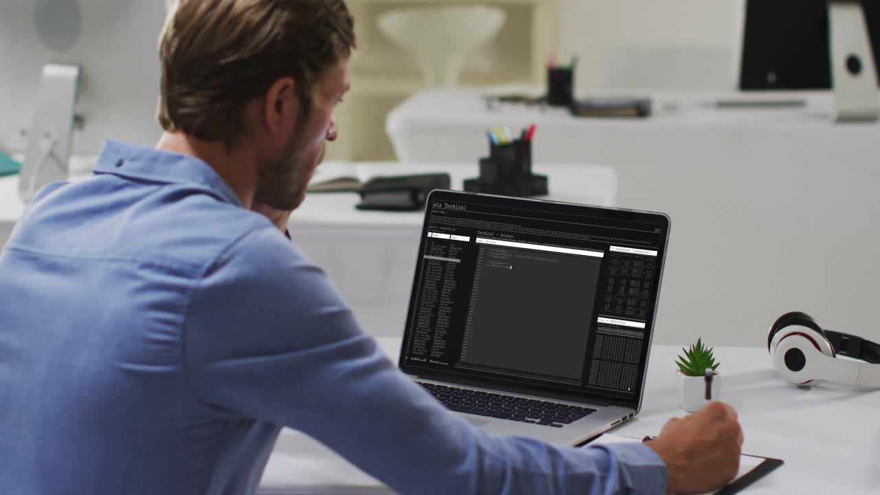 노트북에서 데이터 처리를 코딩하고 메모를 하는 데 책상에 앉아 있는 백인 남자