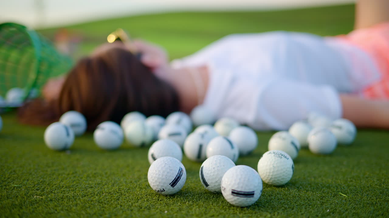 Donna sdraiata sul campo da golf vicino a un secchio con palline rovesciate