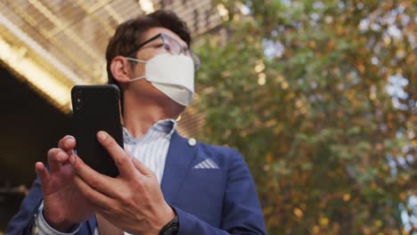 Asian-man-wearing-face-mask-using-smartphone-while-standing-on-the-street