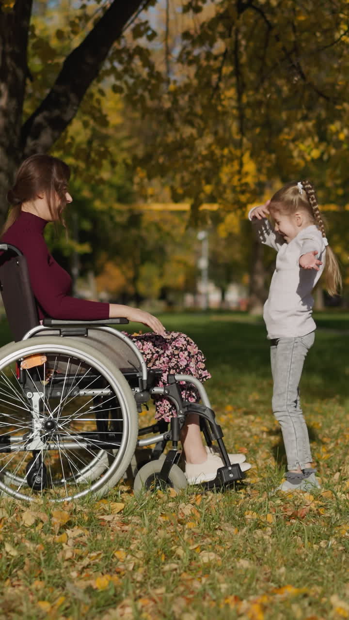 madre joven con lesiones en las piernas lanza un montón de hojas secas por encima de la hija. niña preescolar levanta las manos regocijándose en el juego en el parque de otoño vista lateral