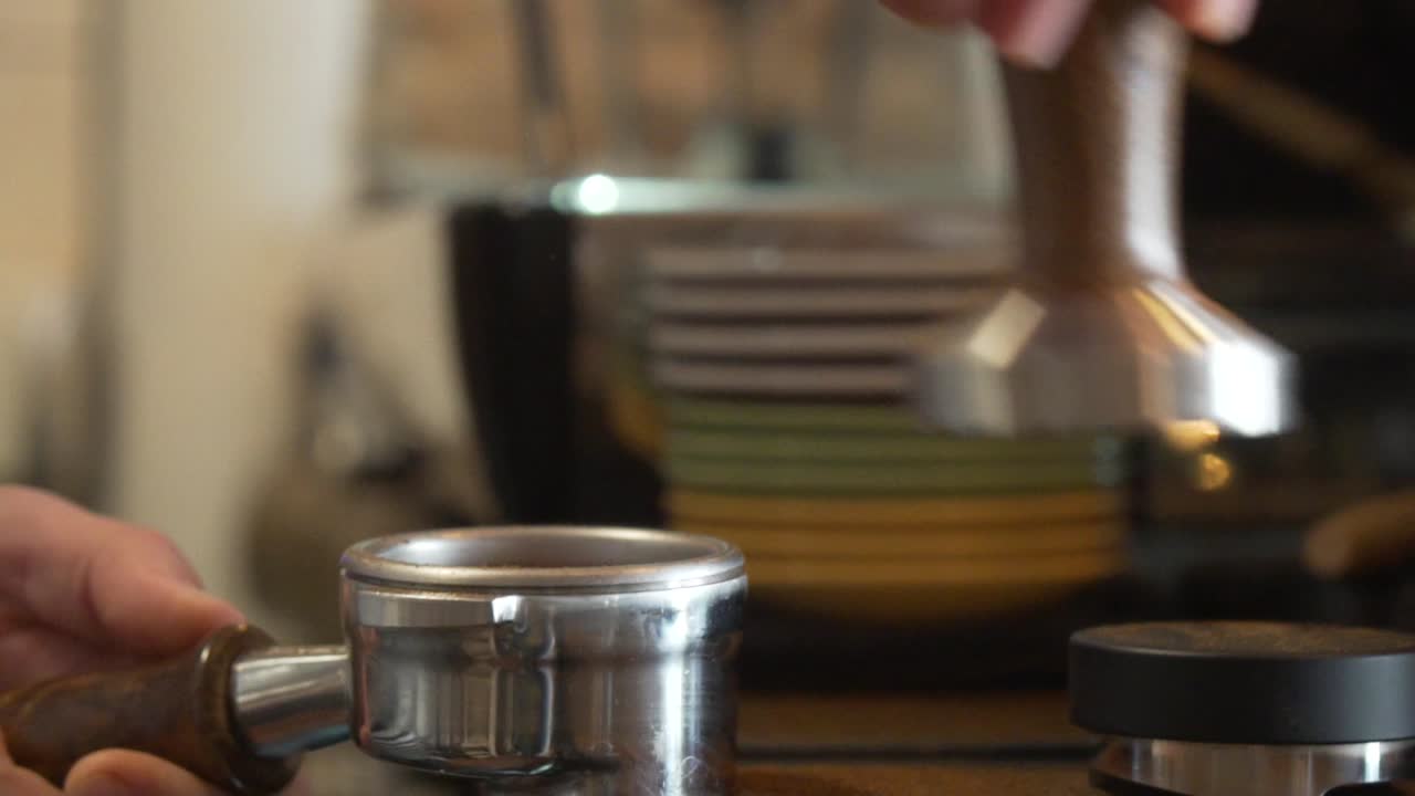 숙련된 바리스타가 탬퍼가 있는 포터필터에 분쇄된 커피를 압착합니다.