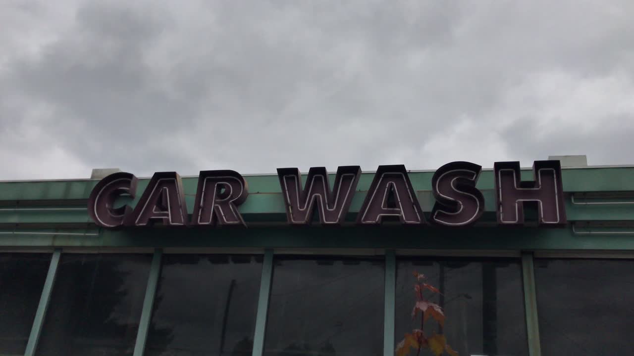 una toma manual de cielos sombríos sobre un letrero de lavado de autos de neón abandonado