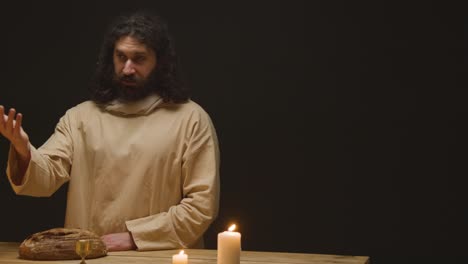 studio shot of man wearing robes with long hair and beard representing figure of jesus christ blessing bread and wine preaching