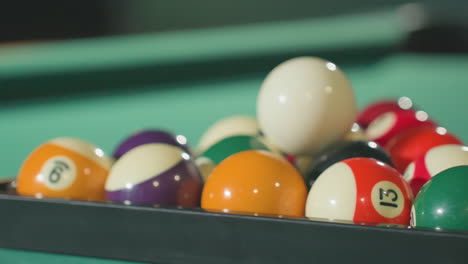 close-up shot of colorful billiard balls arranged neatly in triangle rack on green pool table, showcasing vibrant colors and smooth textures under soft lighting in a relaxed game room setting