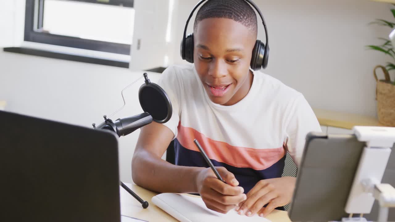 Happy african american male teenage boy recording podcast using laptop, slow motion