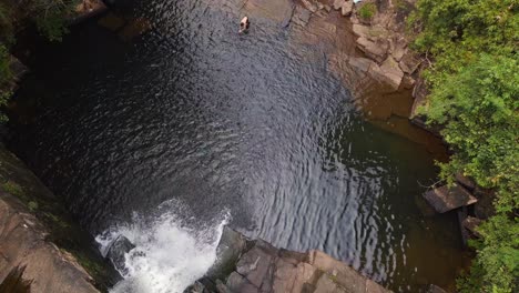 man jumps in lake from waterfall into deep jungle