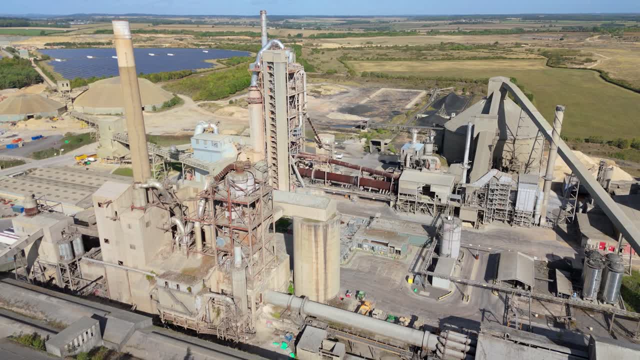 Cinematic drone orbit of cement production facility with chimneys and conveyors near Stamford on a clear day