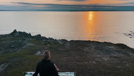 aerial of dreamlike ocean scenery with young attractive woman throwing blanket over herself during sunset in brittany, france