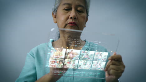 High-tech-concept-of-an-Asian-active-senior-woman-using-a-futuristic-transparent-touchscreen-pad