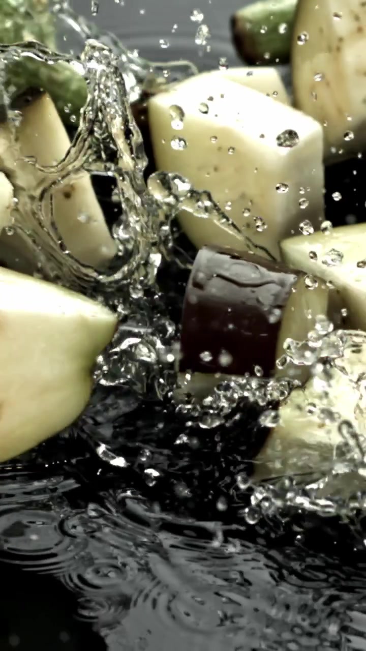 Pezzi di melanzana tritati che schizzano nell'acqua al rallentatore