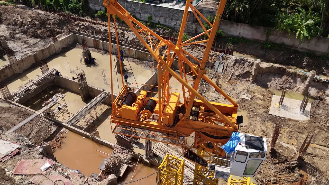 Overhead view of a construction site with a large yellow crane and workers in a muddy excavation