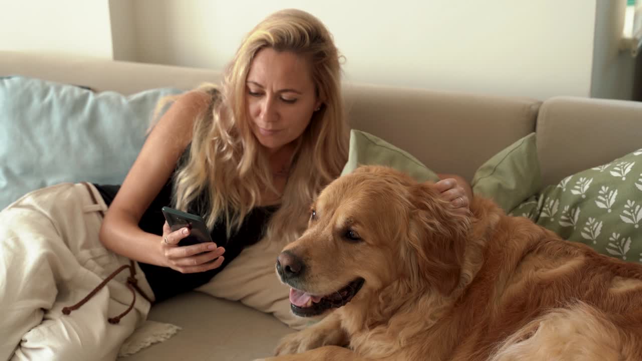 woman using smartphone while sitting with her adorable golden retriever dog