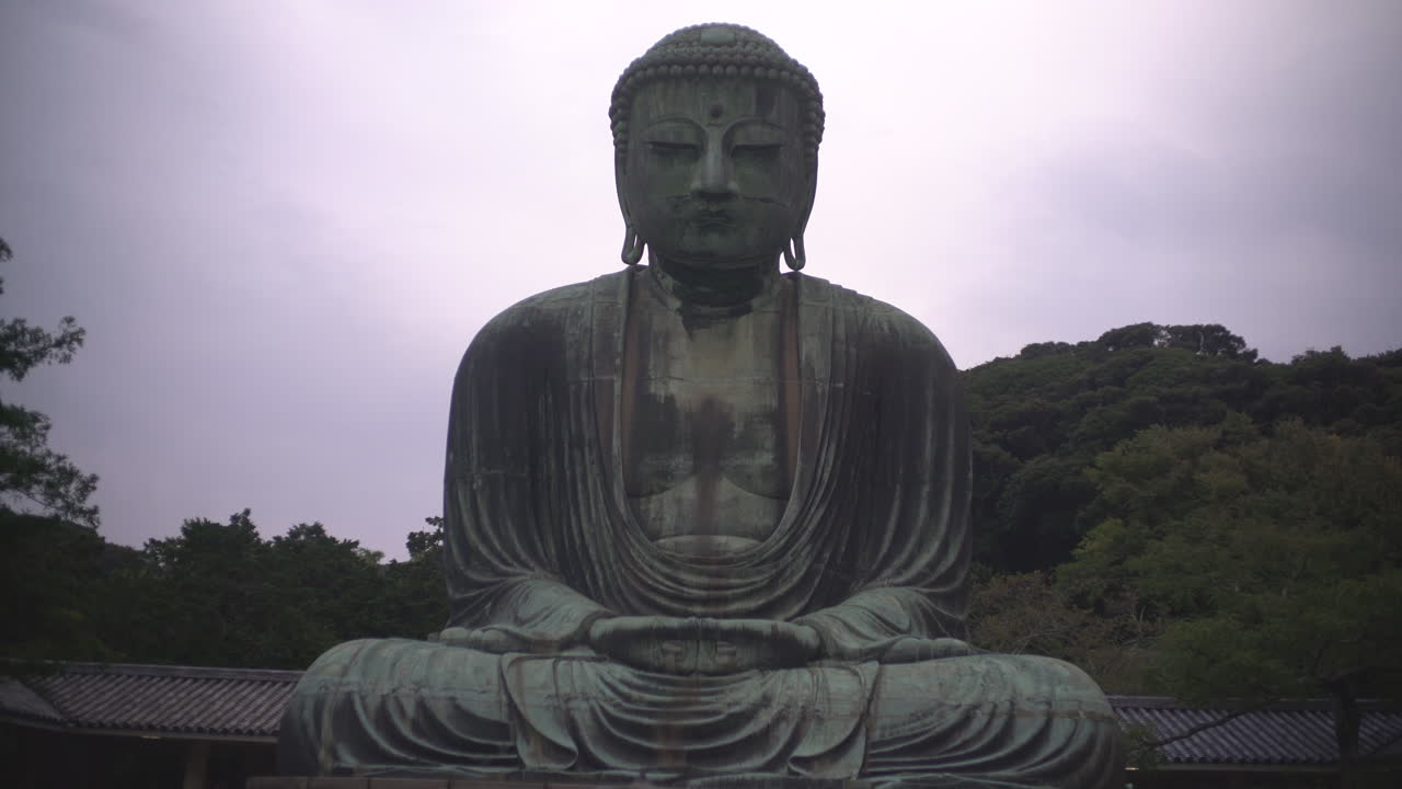 Ripresa a mano libera a figura intera del Grande Buddha di Kamakura seduto in posizione del loto al Tempio Kotoku-in, Giappone. Iconica statua in bronzo del Daibutsu e importante punto di riferimento buddista.