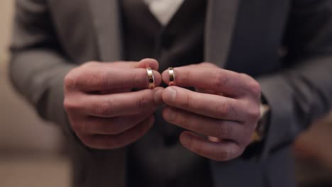 Groom-in-gray-jacket-holding-wedding-rings-on-palm-of-his-hand,-man-touches-the-rings,-slow-motion