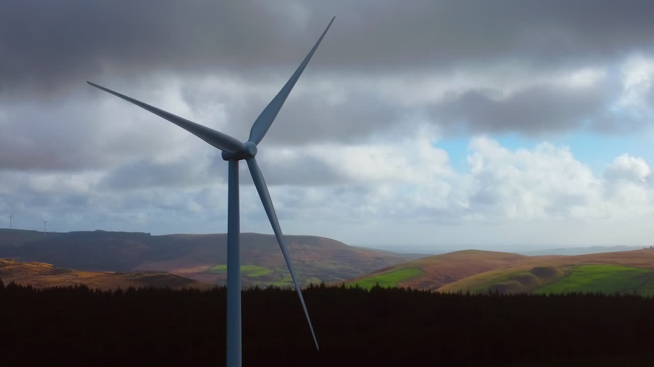 Luftfoto av fjell med vindturbin i rotasjon med solbelyste åser og klar himmel i bakgrunnen. Ren, moderne energiproduksjon. Bærekraftig, fornybar teknologi.