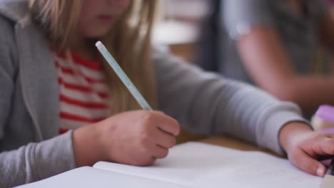 girl writing in a book while sitting on her desk at school