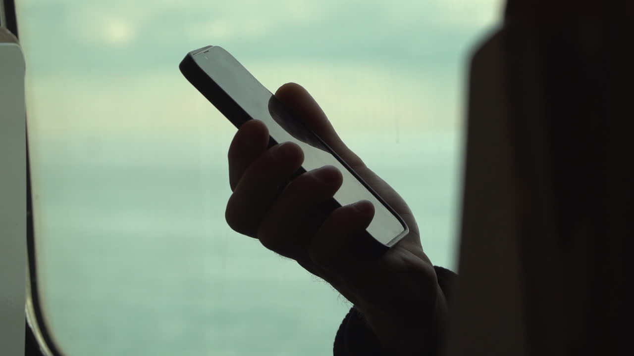 Man holding a phone o the window seat of a moving train