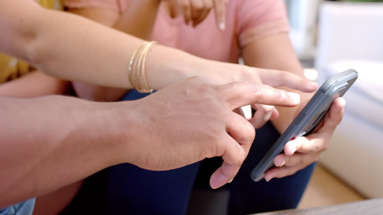 Pointing at smartphone screen, diverse friends discussing something together at home