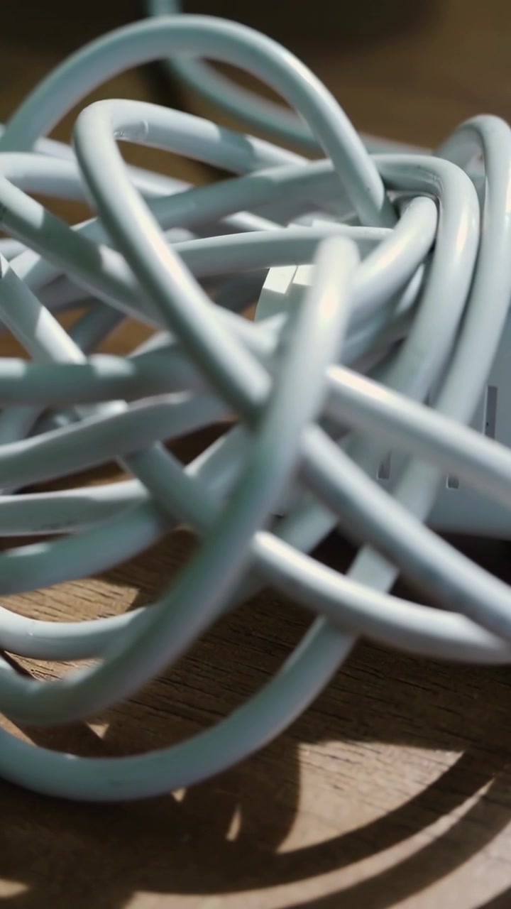 Vertical video: Moving camera showing tangled blue USB cable on wood table, white adapter shadows