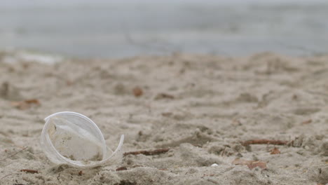 man's hand lifting an empty plastic cup on the beach