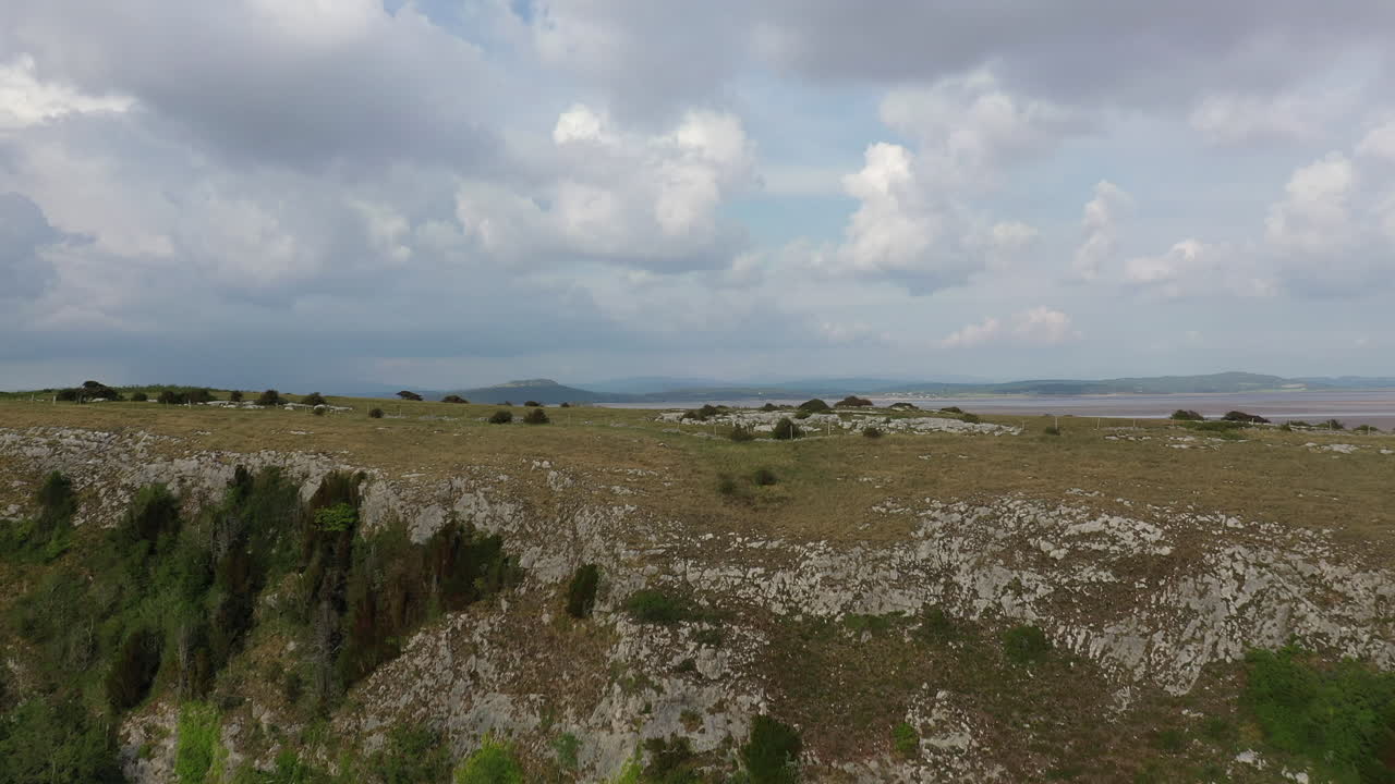 Lenta ripresa aerea che si alza sopra una scogliera, rivelando il paesaggio costiero retrostante, giornata di sole splendente