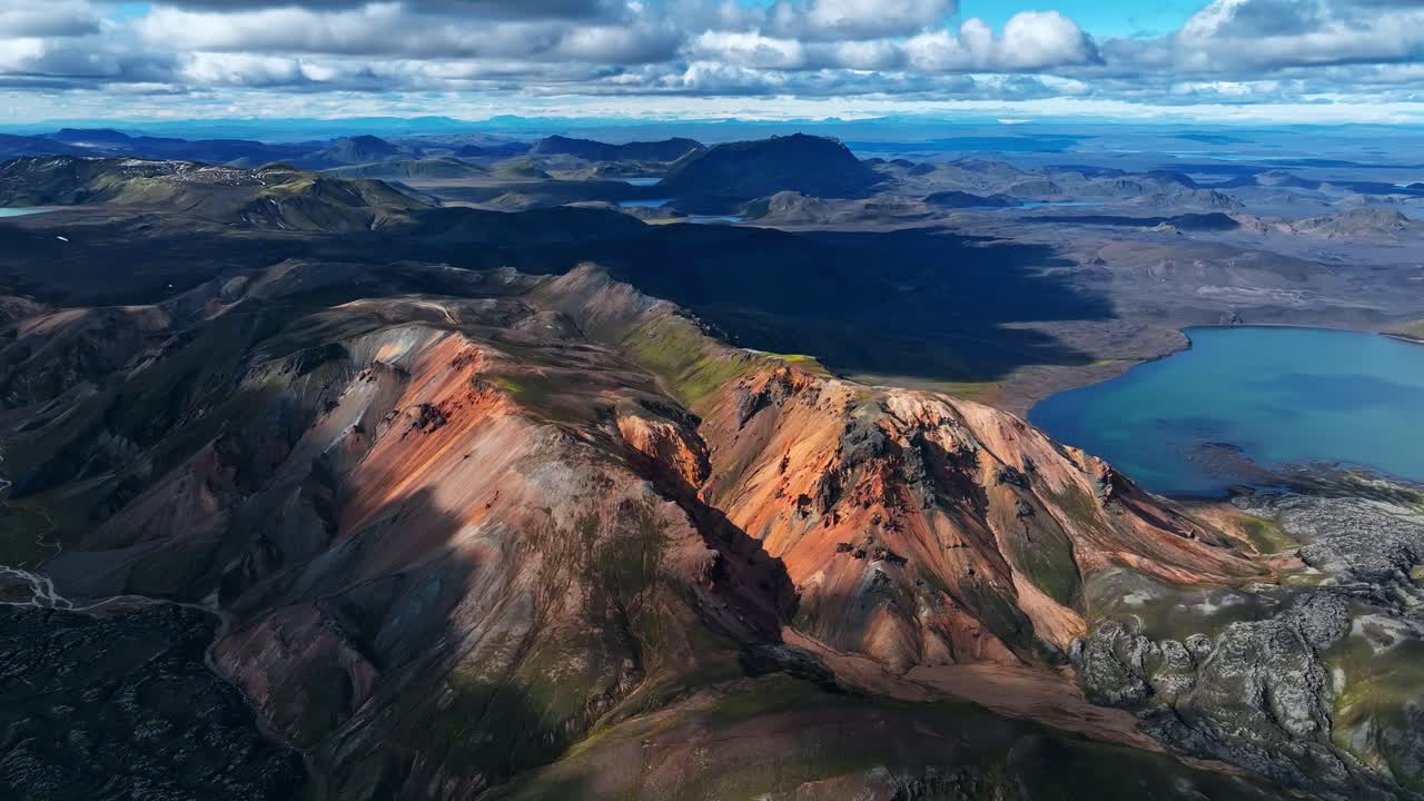 Aerial view of Iceland’s colorful rhyolite mountains, with rugged peaks, deep valleys and a bright lake adding contrast to the volcanic landscape